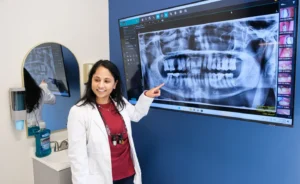Dentist pointing at a panoramic dental X-ray on a large monitor in a dental office.