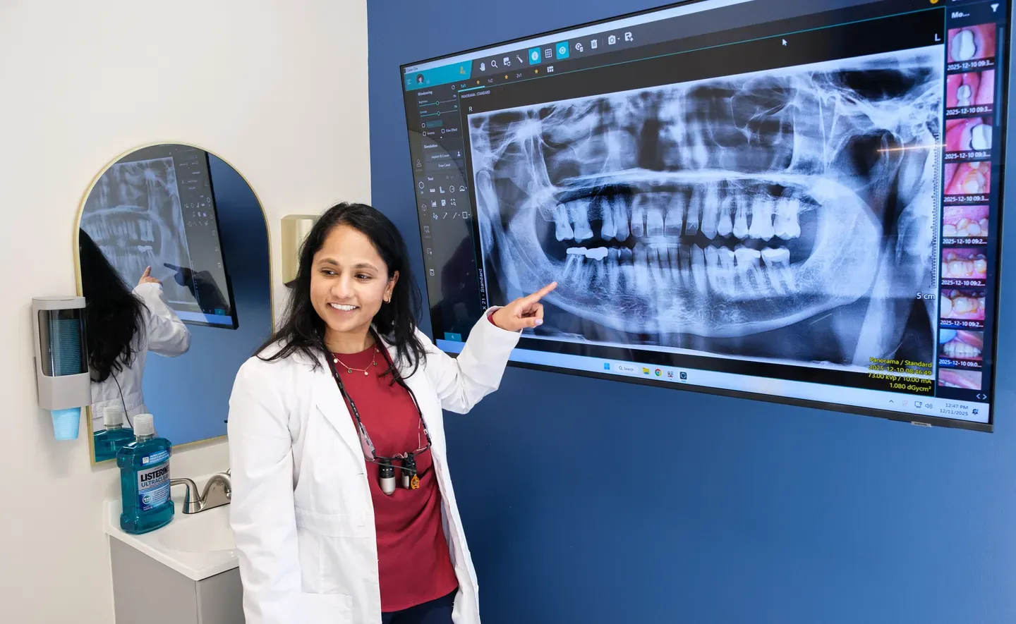 Dentist pointing at a panoramic dental X-ray on a large monitor in a dental office.